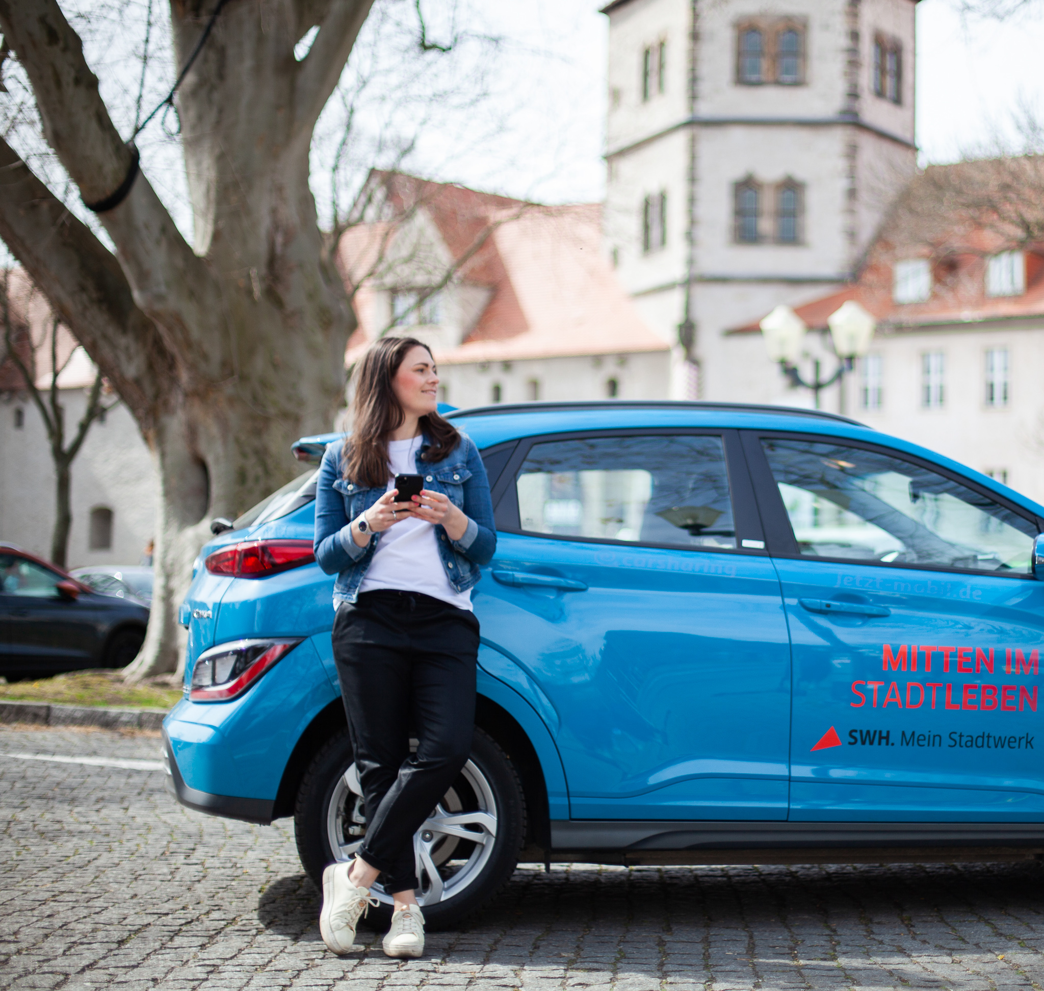 Frau steht auf dem Parkplatz vor dem Museum Moritzburg mit ihrem Smartphone in der Hand.